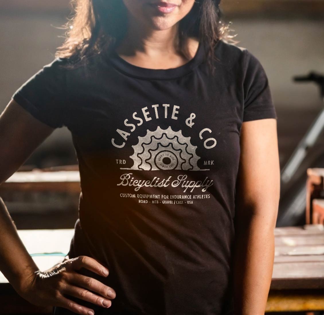 woman wearing black tee with 1 color print in a rustic bike shop