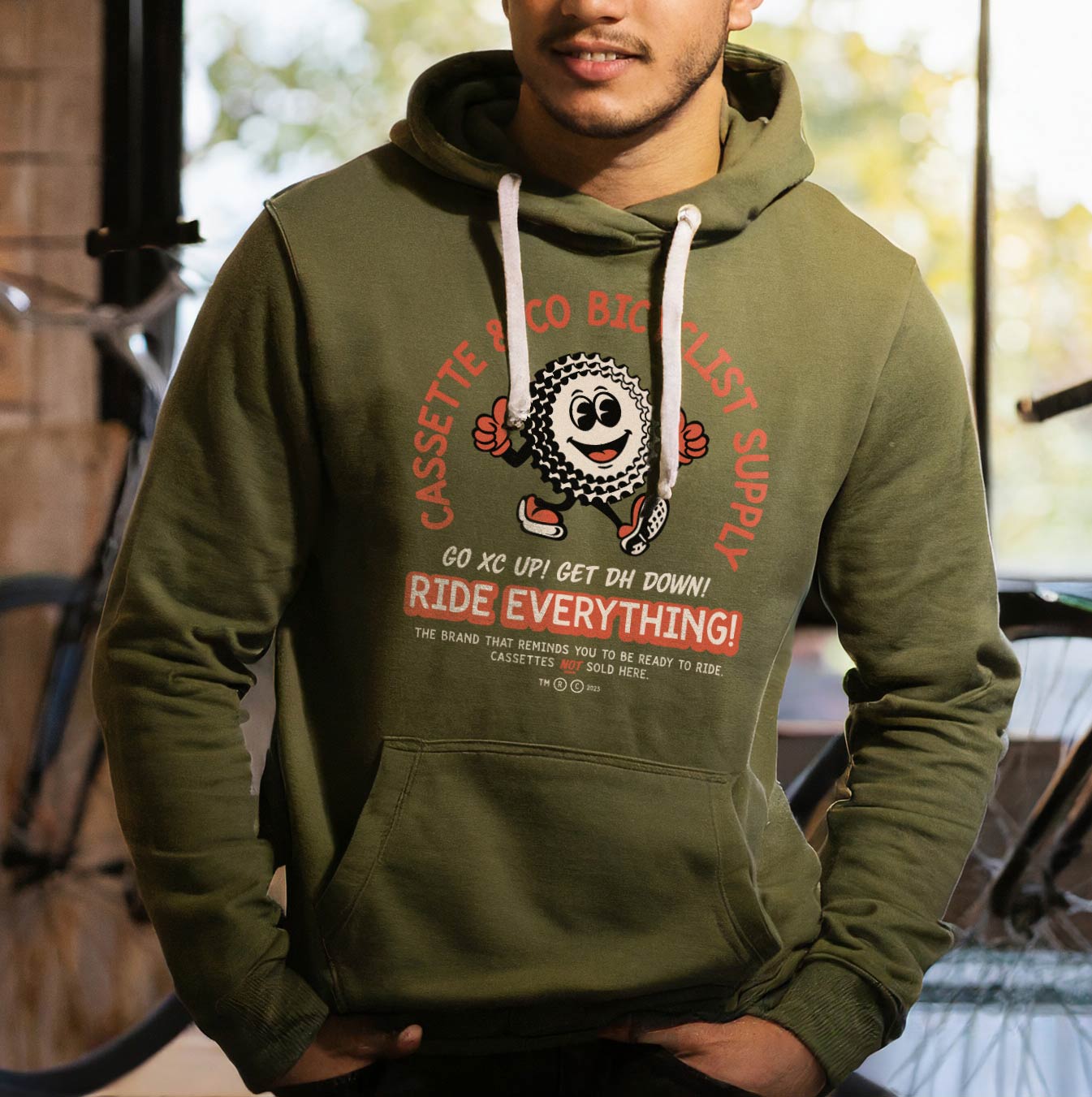 man wearing army green hoodie in a bike shop with 2 color Jonny Cassette print 